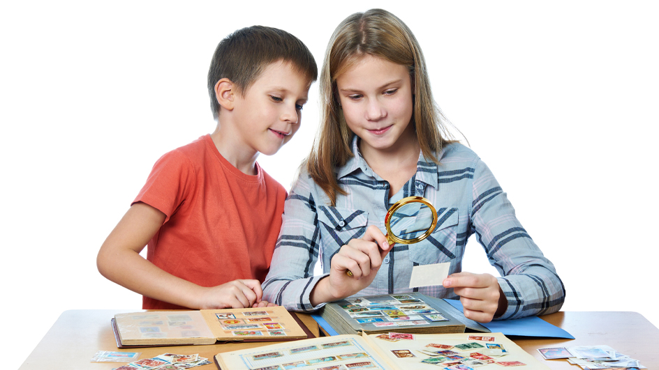 Teen girl and little boy with magnifying glass looking at a book of stamps