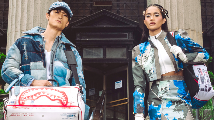 Four people standing on the steps to a large building and holding licensed, USPS-themed backpacks