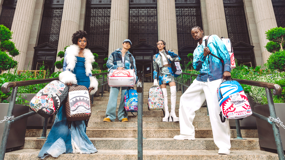 Four people standing on the steps to a large building and holding licensed, USPS-themed backpacks