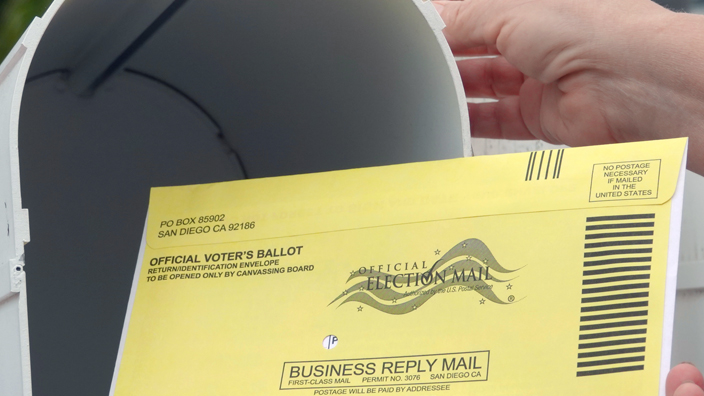 Closeup of a yellow envelope with the Election Mail logo being put into a mailbox