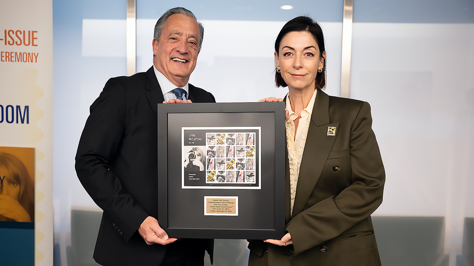 A man and a woman standing side-by-side and holding framed Linda McCartney stamps