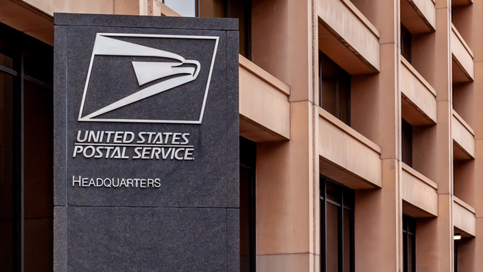 Exterior of USPS headquarters building and a large, black column bearing the Postal Service logo