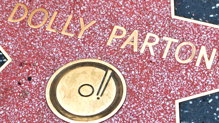 Image of a red star on a sidewalk with the name “Dolly Parton” and a music record icon inside of it