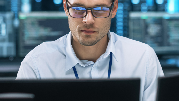 Man wearing eyeglasses and a white button-up shirt sitting behind a computer monitor