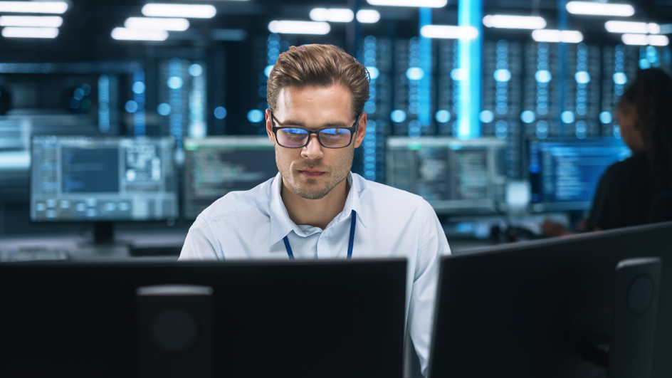 Man wearing eyeglasses and a white button-up shirt sitting behind a computer monitor