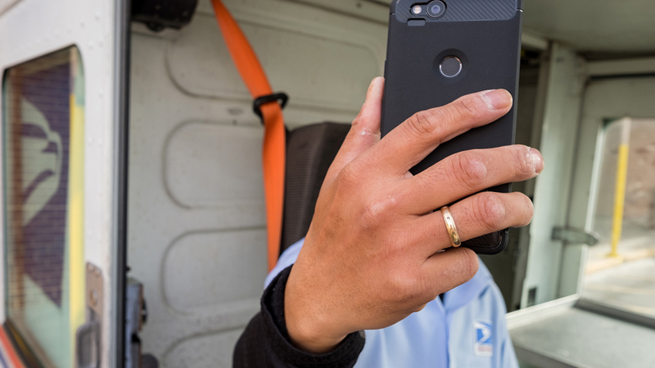 USPS employee sitting in a delivery vehicle holding up a cellphone in front of their face