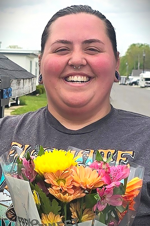 Close-up of a woman in a gray T-shirt standing outdoors and holding a bouquet of wildflowers