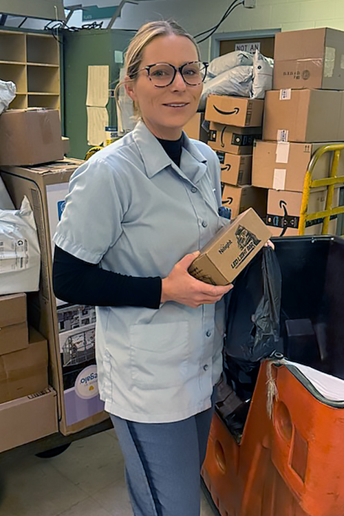 A uniformed USPS employee standing in a Post Office work area and holding a package