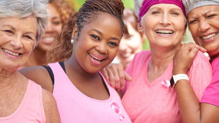 A group of women embracing one another and wearing pink shirts and pink ribbons