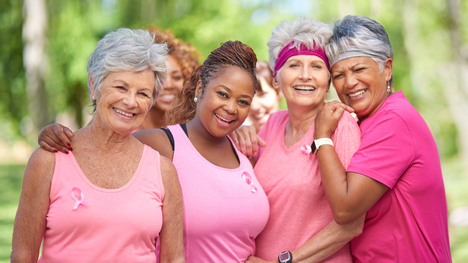A group of women embracing one another and wearing pink shirts and pink ribbons