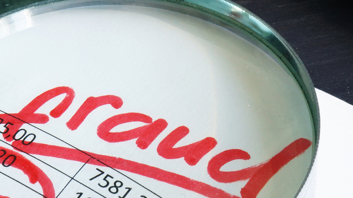 A spreadsheet of numbers with a magnifying glass on top magnifying the word fraud written in red marker
