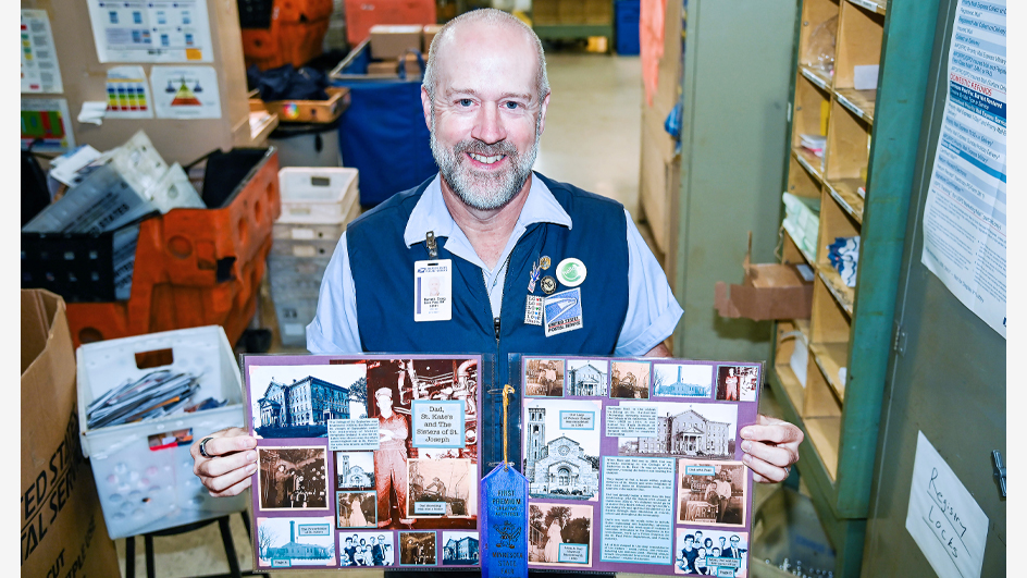 A smiling uniformed USPS employee holds up pages from a scrapbook