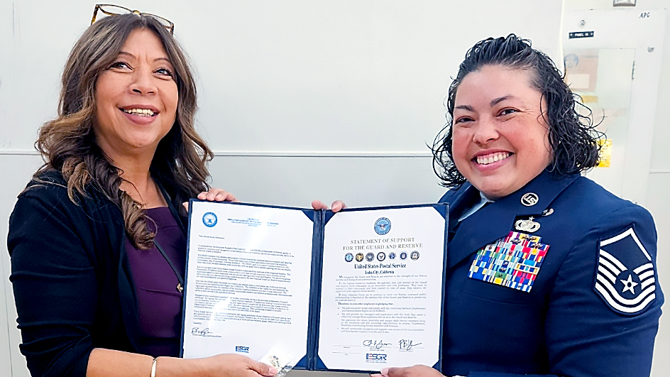 A woman in business attire and a woman in a U.S. Air Force uniform standing side by side and holding up an award